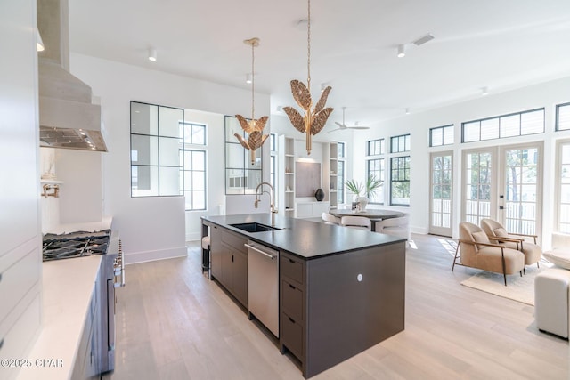 kitchen featuring light wood-style flooring, open floor plan, stainless steel appliances, wall chimney range hood, and a sink