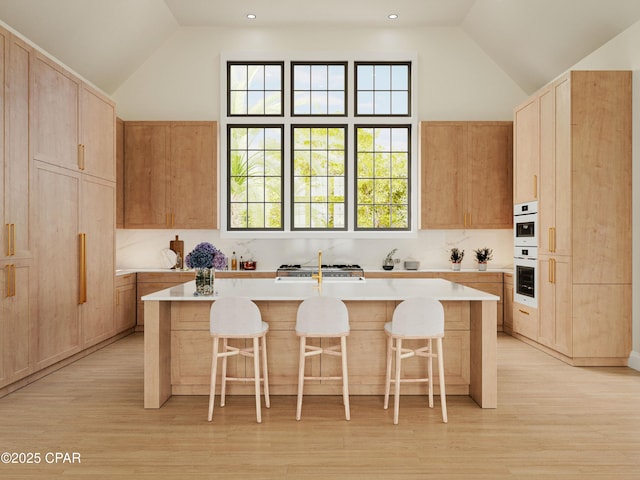 kitchen with a breakfast bar, an island with sink, light brown cabinets, and light countertops