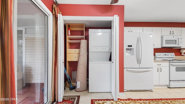 kitchen featuring light tile patterned floors, white cabinetry, white appliances, and stacked washing maching and dryer