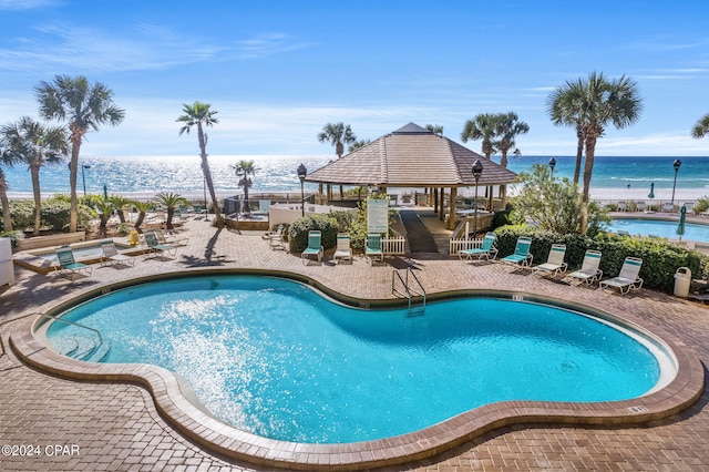 pool with a gazebo, a water view, a hot tub, and a patio