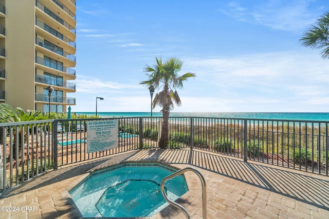 view of pool with fence, a water view, and a hot tub