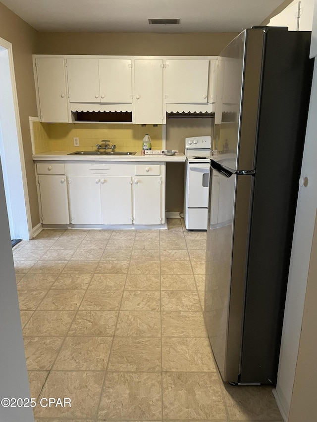 kitchen with white range with electric stovetop, visible vents, freestanding refrigerator, white cabinetry, and a sink