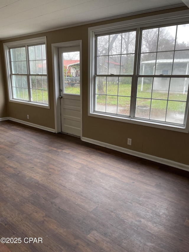 spare room featuring dark wood-type flooring, a healthy amount of sunlight, and baseboards