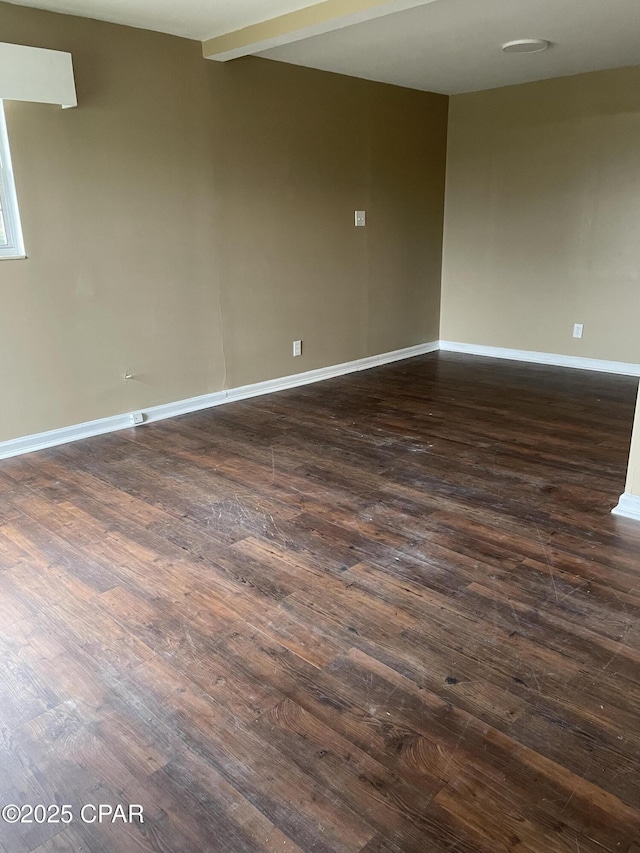 empty room featuring dark wood-style floors, beamed ceiling, and baseboards