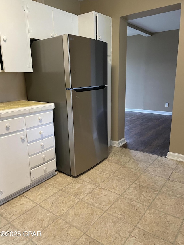 kitchen with tile countertops, baseboards, freestanding refrigerator, and white cabinets