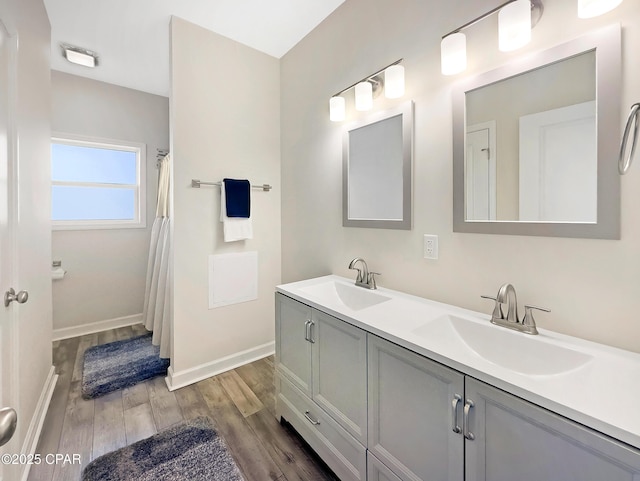 full bathroom featuring double vanity, wood finished floors, a sink, and baseboards