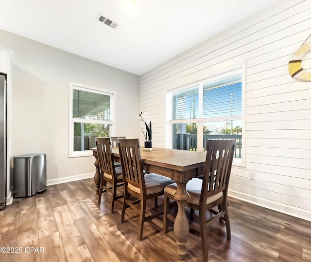 dining space with baseboards, wood finished floors, visible vents, and wooden walls