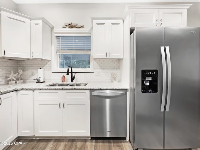 kitchen featuring light wood-style flooring, stainless steel appliances, a sink, white cabinetry, and tasteful backsplash