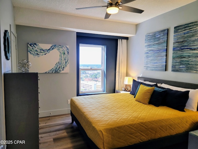 bedroom featuring a ceiling fan, a textured ceiling, baseboards, and wood finished floors