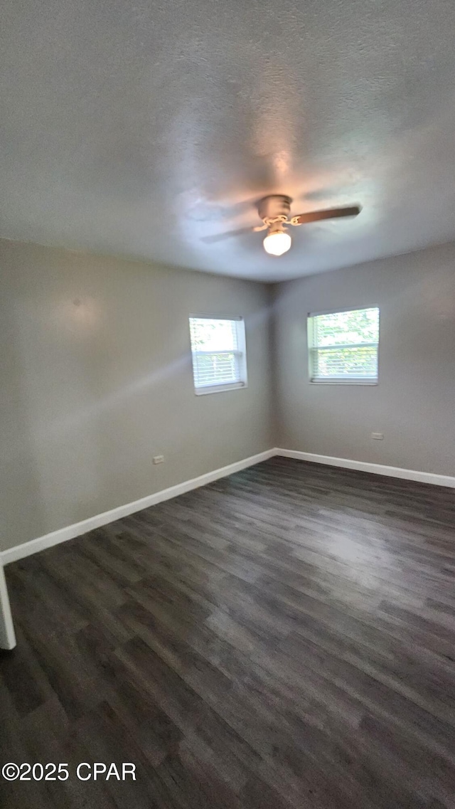 empty room featuring baseboards, dark wood-type flooring, a ceiling fan, and a textured ceiling