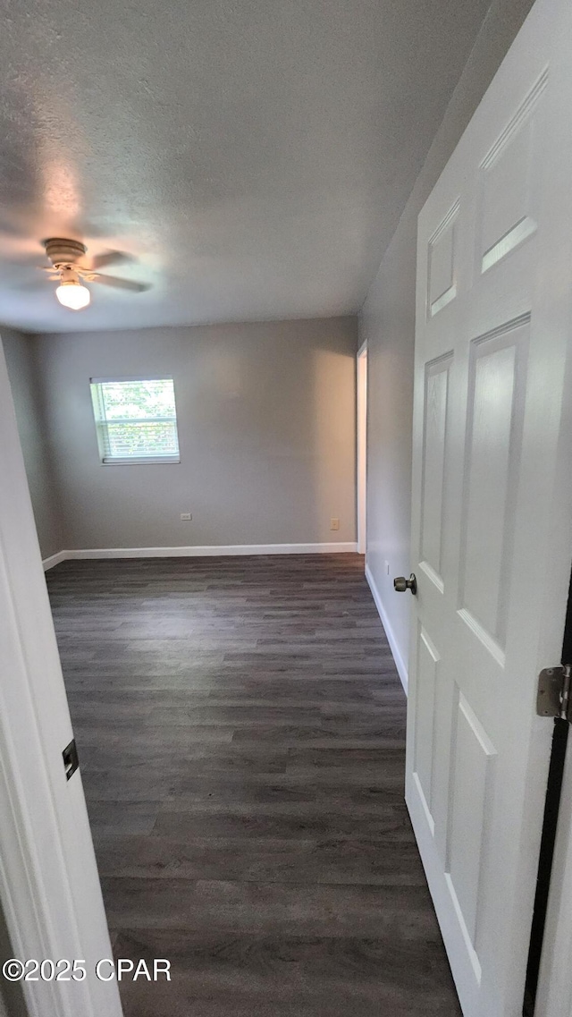 empty room with dark wood finished floors, ceiling fan, a textured ceiling, and baseboards