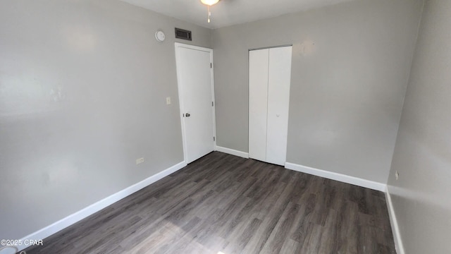 unfurnished bedroom featuring a closet, baseboards, visible vents, and dark wood finished floors