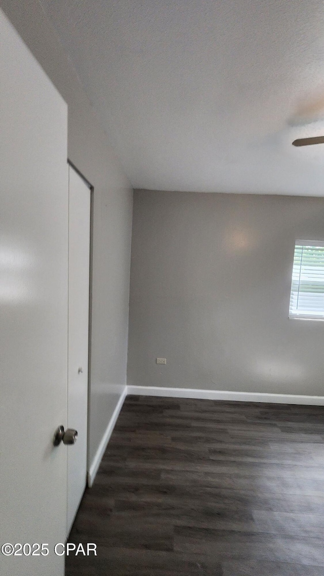 spare room featuring baseboards, dark wood finished floors, and a ceiling fan