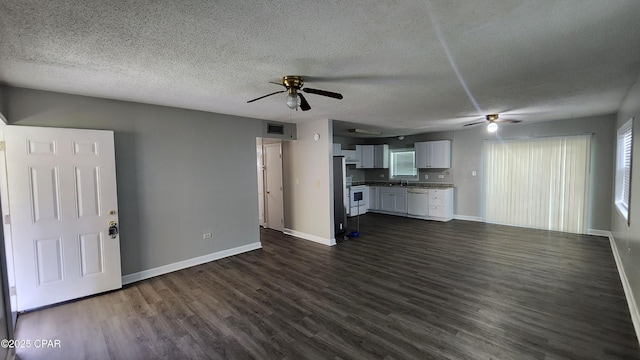 unfurnished living room with visible vents, dark wood-type flooring, a textured ceiling, baseboards, and ceiling fan