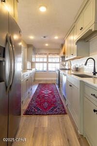 kitchen with stainless steel refrigerator with ice dispenser, recessed lighting, light countertops, a sink, and wood finished floors