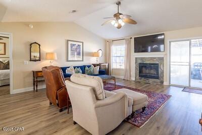 living room with light wood-type flooring, lofted ceiling, a glass covered fireplace, and ceiling fan