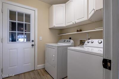 clothes washing area featuring washing machine and dryer, baseboards, cabinet space, and light wood finished floors