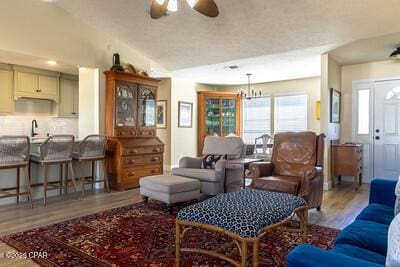 living area with ceiling fan with notable chandelier, vaulted ceiling, and wood finished floors