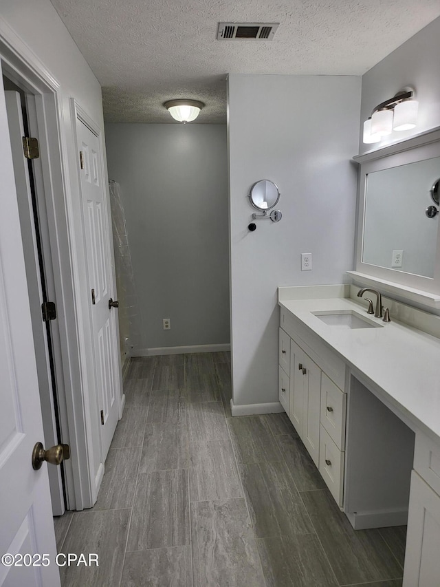 bathroom with visible vents, a textured ceiling, vanity, and baseboards