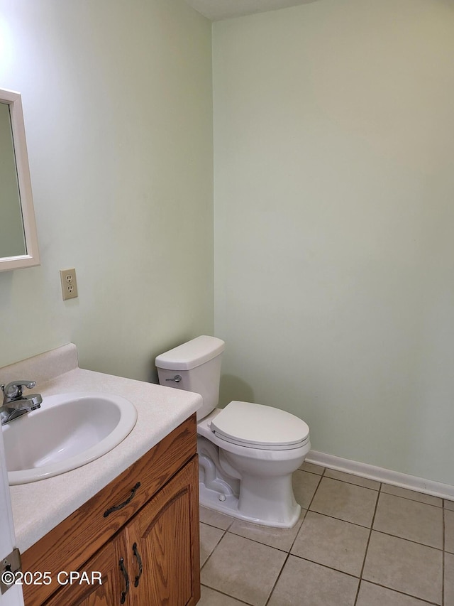 half bathroom with tile patterned flooring, baseboards, vanity, and toilet