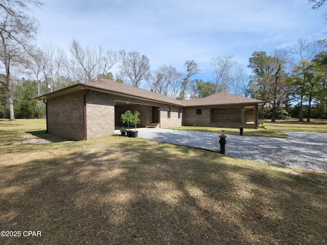 view of front of house with gravel driveway, brick siding, a front yard, a patio area, and a garage