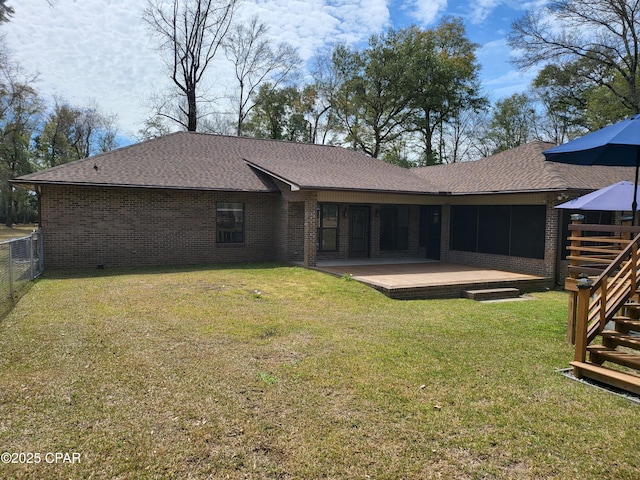 rear view of house with a deck, brick siding, fence, roof with shingles, and a lawn