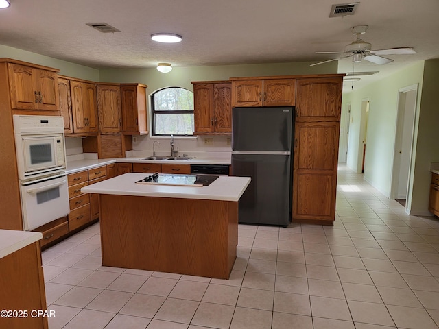 kitchen with electric stovetop, a sink, visible vents, freestanding refrigerator, and brown cabinetry