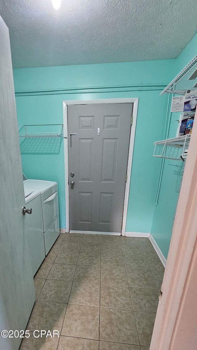 laundry area with washing machine and clothes dryer, a textured ceiling, tile patterned flooring, laundry area, and baseboards