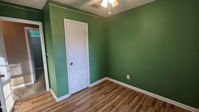 unfurnished bedroom with baseboards, visible vents, ceiling fan, wood finished floors, and a closet