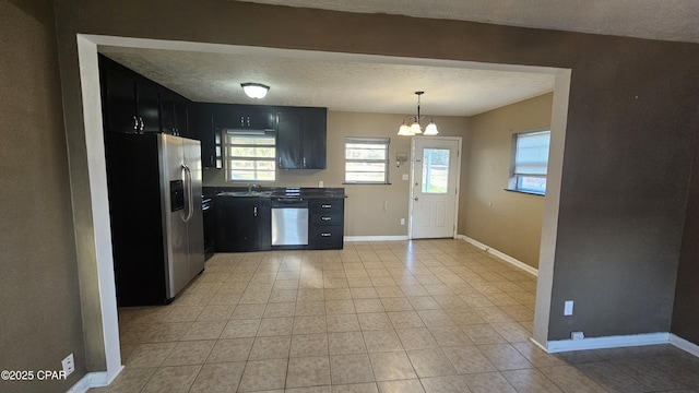 kitchen featuring a textured ceiling, stainless steel appliances, a sink, baseboards, and dark cabinetry