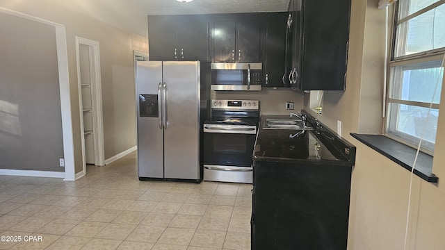 kitchen with light tile patterned floors, appliances with stainless steel finishes, a sink, dark cabinets, and baseboards