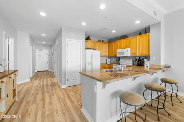 kitchen with a peninsula, white appliances, a kitchen breakfast bar, and light wood finished floors