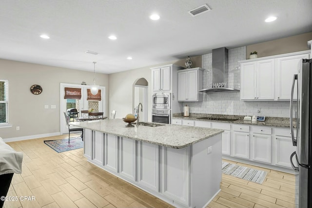 kitchen with a sink, visible vents, appliances with stainless steel finishes, backsplash, and wall chimney exhaust hood