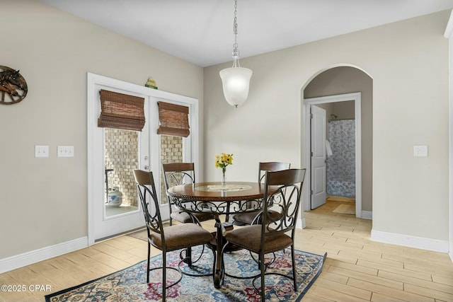 dining room featuring arched walkways, baseboards, and light wood-style floors