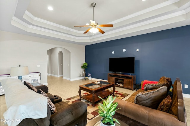 living area with arched walkways, ornamental molding, a raised ceiling, and baseboards