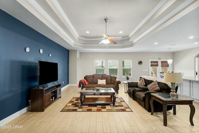 living area featuring crown molding, light wood finished floors, a raised ceiling, ceiling fan, and baseboards