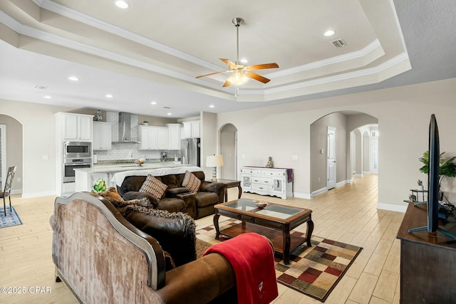 living area with arched walkways, a raised ceiling, visible vents, and light wood-style floors