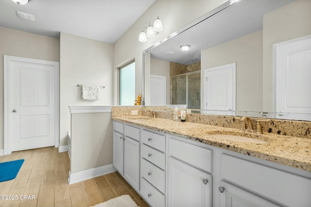 bathroom with double vanity, wood finished floors, a stall shower, and a sink