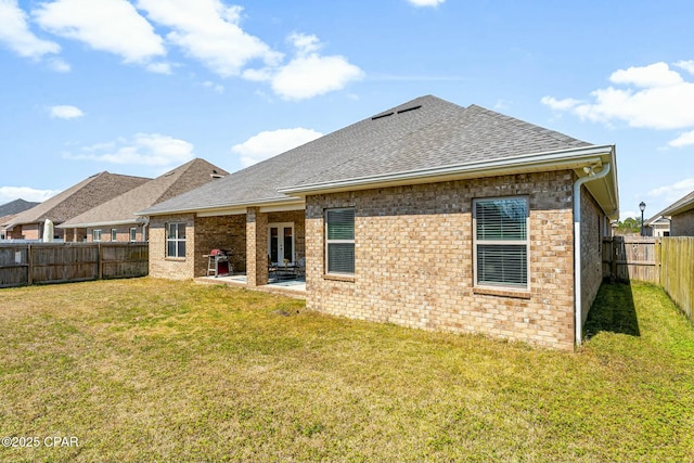 back of property featuring a patio, a fenced backyard, roof with shingles, a yard, and brick siding