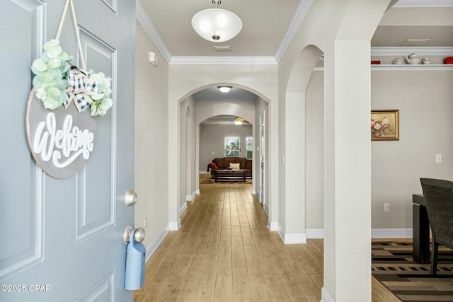 corridor featuring arched walkways, light wood finished floors, visible vents, ornamental molding, and baseboards