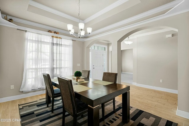 dining space featuring light wood-style floors, a tray ceiling, a chandelier, and arched walkways