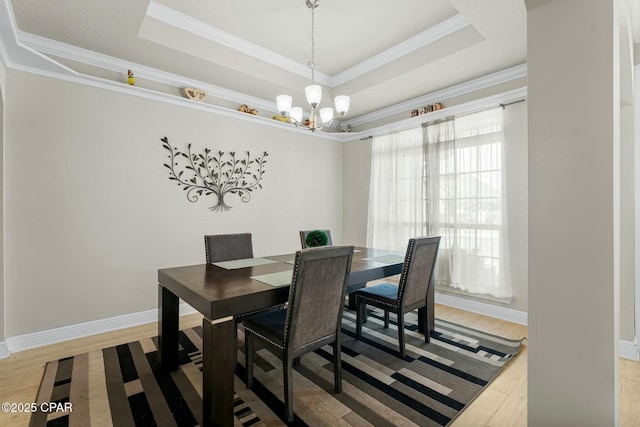 dining room with ornamental molding, a tray ceiling, light wood-type flooring, and baseboards