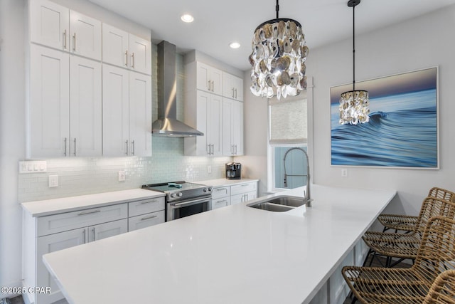 kitchen with a breakfast bar, a sink, stainless steel range with electric cooktop, wall chimney exhaust hood, and tasteful backsplash