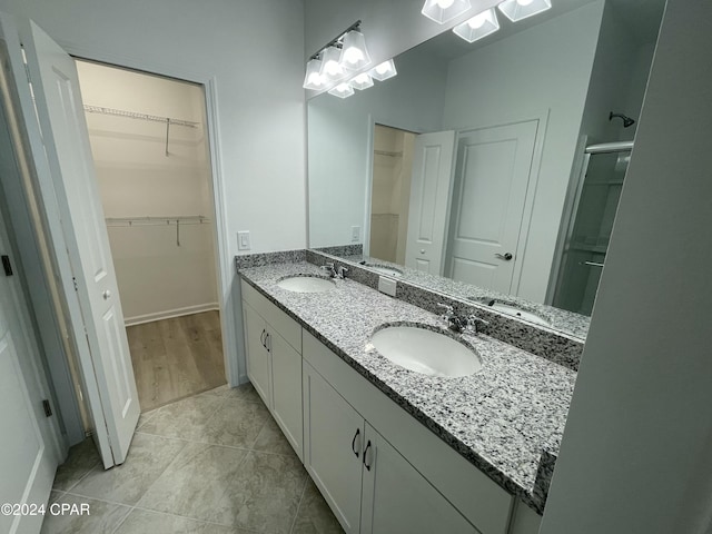 full bathroom featuring double vanity, a sink, a walk in closet, and a shower stall