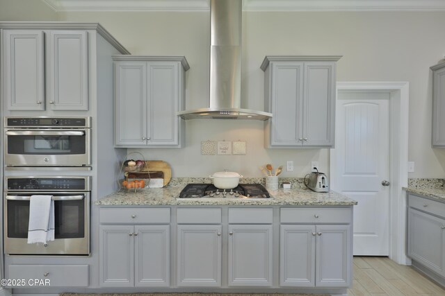 146 Bayou Manor Rd, Santa Rosa Beach, FL 32459 - kitchen featuring light stone counters, appliances with stainless steel finishes, light wood-style flooring, wall chimney range hood, and ornamental molding