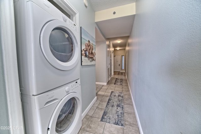 laundry room with light tile patterned floors, baseboards, stacked washing maching and dryer, laundry area, and a textured ceiling