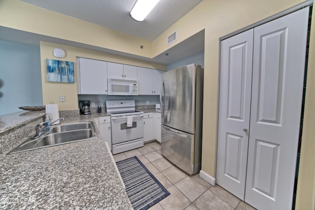 kitchen with visible vents, a sink, white appliances, white cabinets, and light tile patterned floors