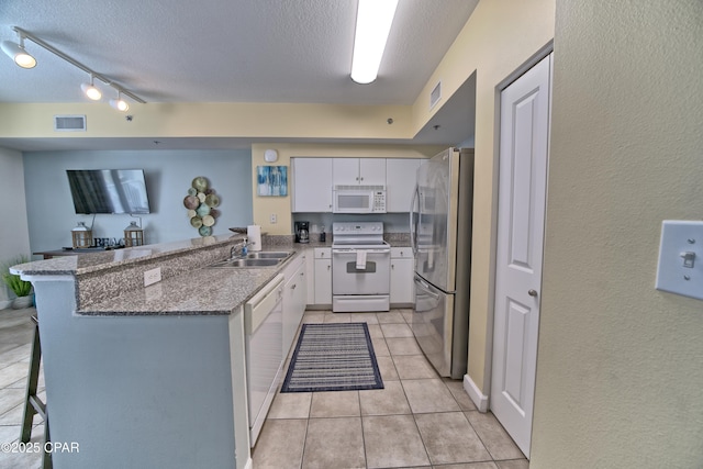 kitchen with a sink, visible vents, white appliances, and a peninsula