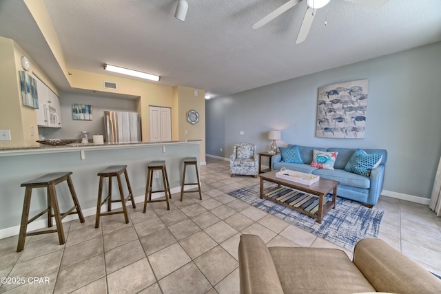 living area with light tile patterned floors, visible vents, a textured ceiling, and a ceiling fan