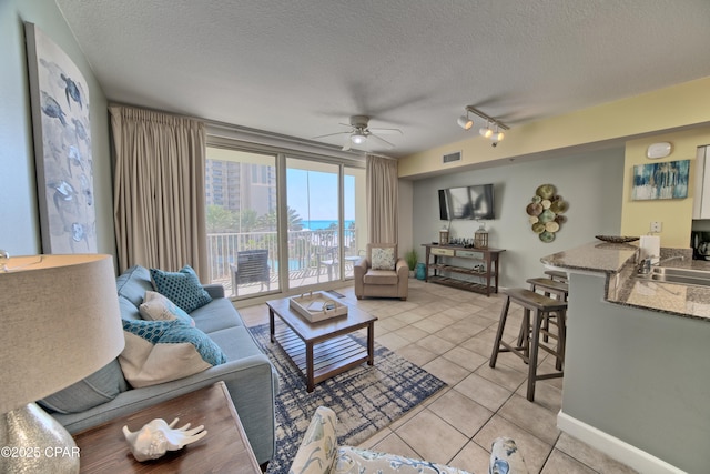 living room featuring a textured ceiling, ceiling fan, light tile patterned flooring, visible vents, and baseboards